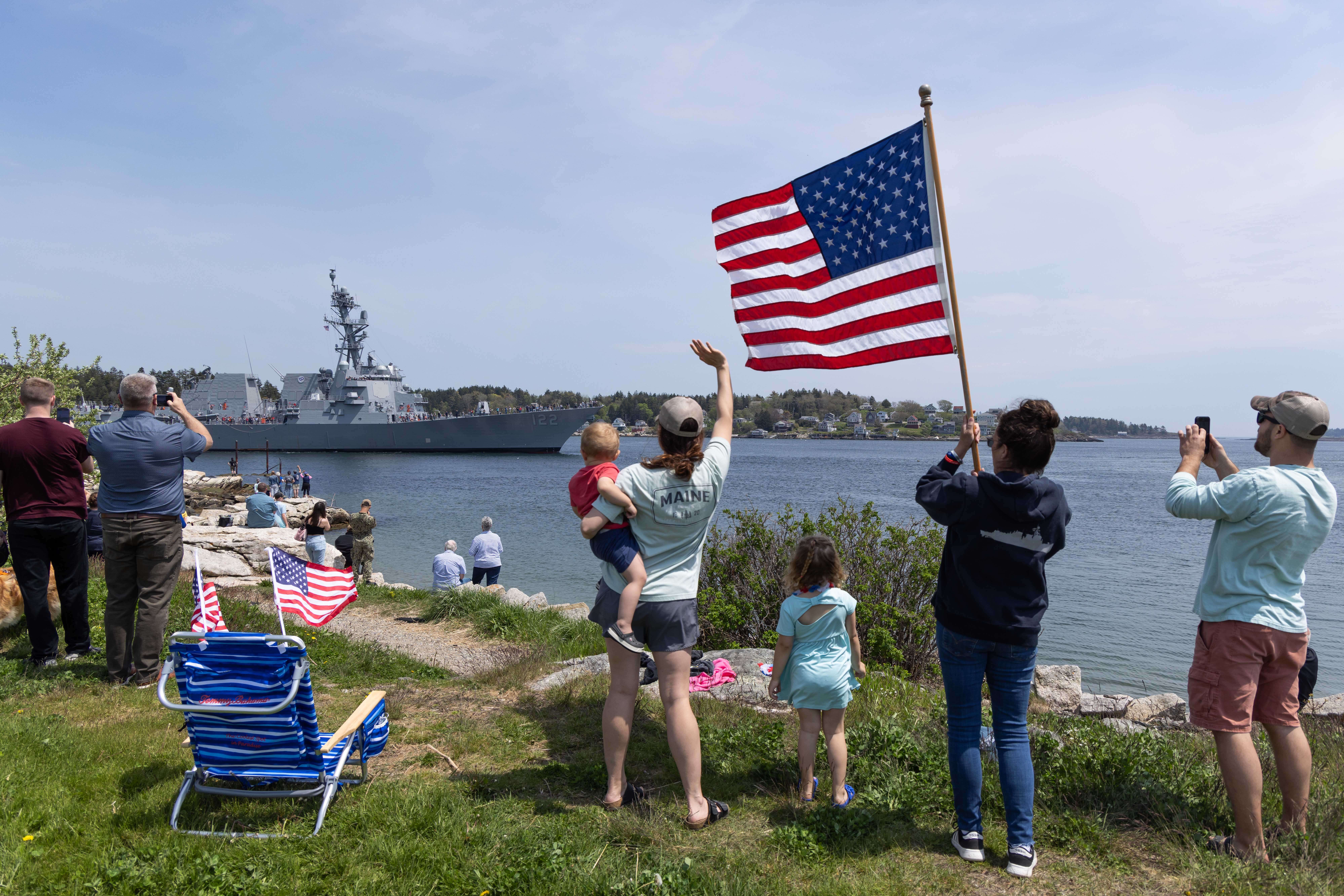 Onlookers wave and hold up American flag for John Basilone (DDG 122)
