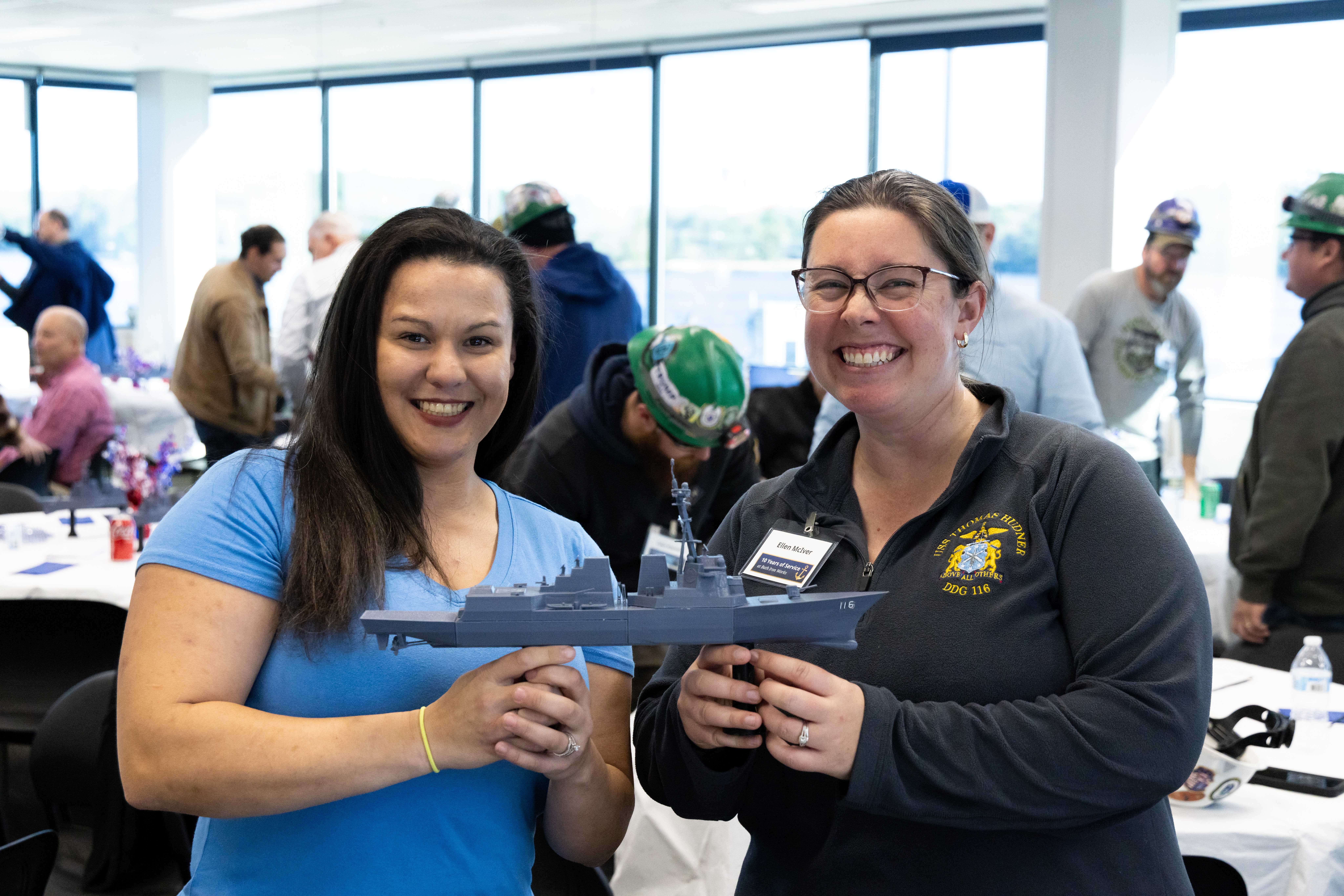 Two BIW shipbuilders hold up a model DDG 51 during a service anniversary luncheon